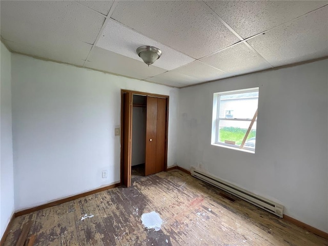 unfurnished bedroom with a drop ceiling, a closet, wood-type flooring, and a baseboard radiator