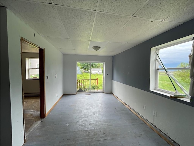 empty room with a paneled ceiling, a healthy amount of sunlight, and baseboard heating