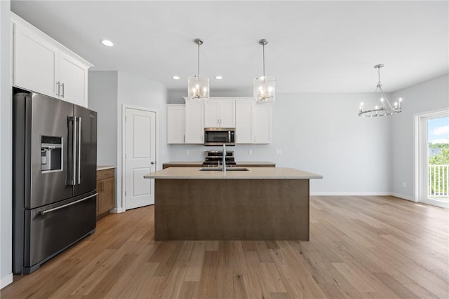 kitchen featuring a kitchen island with sink, white cabinets, hanging light fixtures, light hardwood / wood-style flooring, and stainless steel appliances