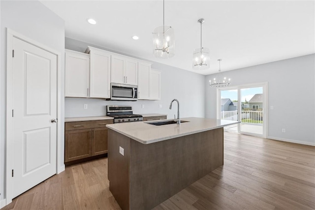 kitchen featuring white cabinets, sink, light wood-type flooring, decorative light fixtures, and stainless steel appliances