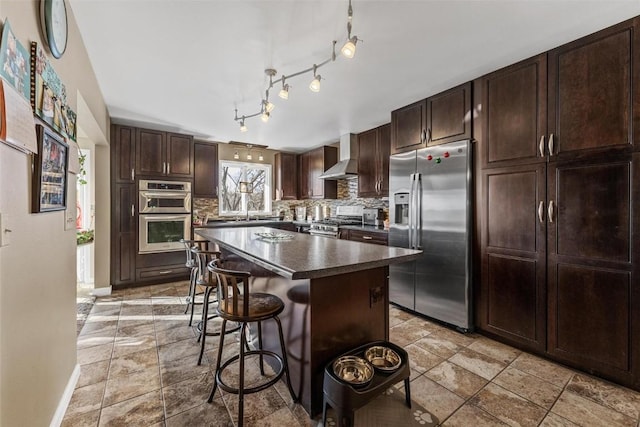 kitchen featuring a breakfast bar, a center island, backsplash, wall chimney range hood, and stainless steel appliances