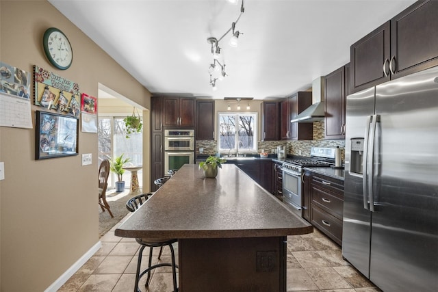 kitchen featuring stainless steel appliances, dark countertops, backsplash, a healthy amount of sunlight, and wall chimney exhaust hood