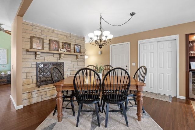 dining space with ceiling fan with notable chandelier, a stone fireplace, baseboards, and wood finished floors