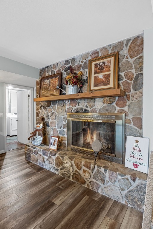 room details with washer / dryer, a stone fireplace, and wood finished floors