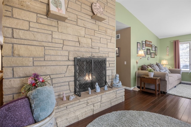 living room featuring visible vents, vaulted ceiling, a stone fireplace, wood finished floors, and baseboards