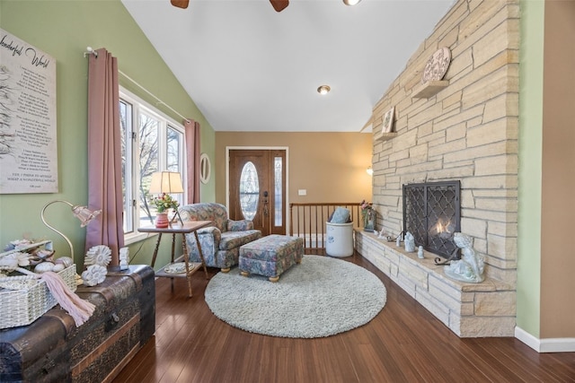 living area featuring lofted ceiling, ceiling fan, a stone fireplace, baseboards, and dark wood-style floors