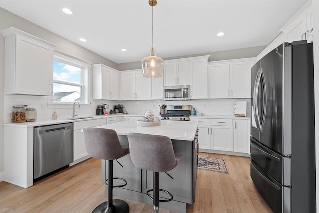 kitchen featuring sink, hanging light fixtures, light hardwood / wood-style floors, white cabinets, and appliances with stainless steel finishes