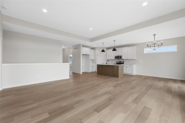 unfurnished living room with light hardwood / wood-style floors, a chandelier, and sink