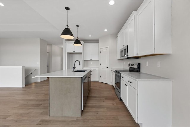 kitchen with pendant lighting, stainless steel appliances, a kitchen island with sink, white cabinetry, and sink