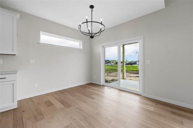 unfurnished dining area with a notable chandelier and light wood-type flooring