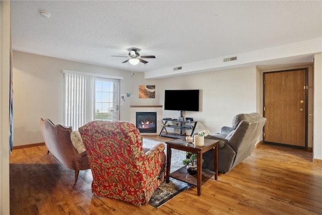 living room featuring a tile fireplace, ceiling fan, and wood-type flooring