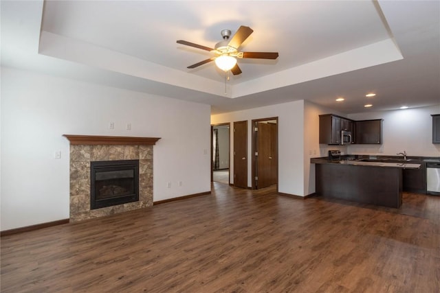 unfurnished living room with a tray ceiling, ceiling fan, a fireplace, and dark wood-type flooring