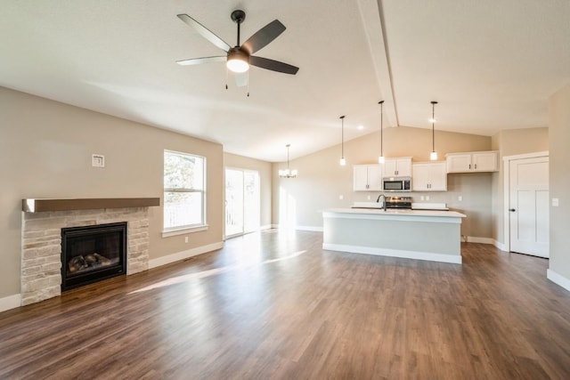 unfurnished living room with dark wood finished floors, lofted ceiling, a stone fireplace, baseboards, and ceiling fan with notable chandelier