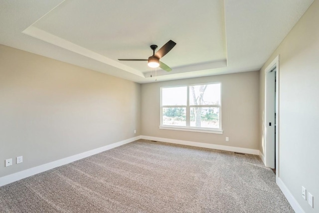 unfurnished room featuring a raised ceiling, ceiling fan, and carpet flooring