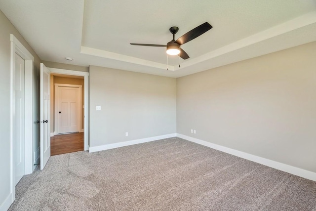 carpeted spare room featuring a tray ceiling, a ceiling fan, and baseboards