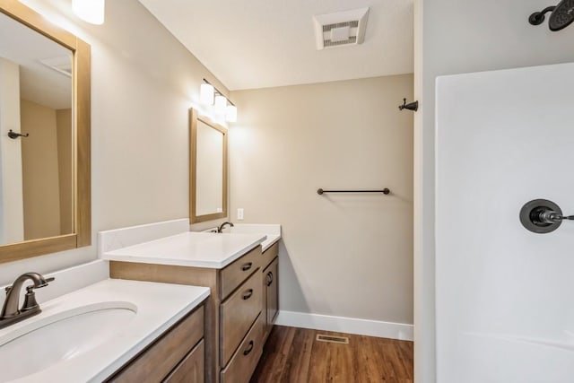 bathroom featuring wood finished floors, two vanities, a sink, visible vents, and baseboards