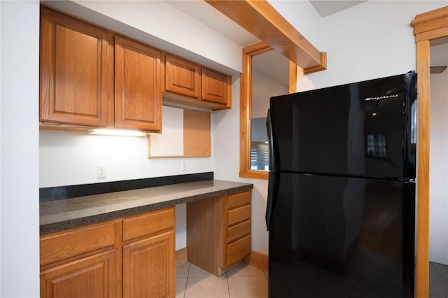 kitchen with black refrigerator, built in desk, and light tile patterned floors