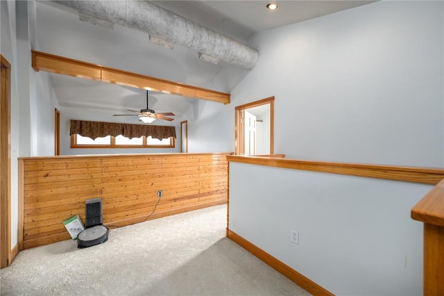 carpeted spare room with lofted ceiling, ceiling fan, and wood walls