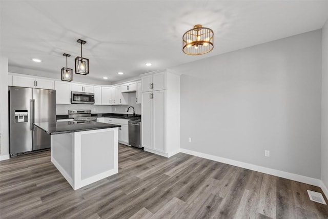 kitchen with stainless steel appliances, white cabinetry, light hardwood / wood-style floors, a kitchen island, and hanging light fixtures