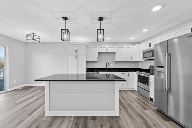 kitchen featuring pendant lighting, stainless steel appliances, white cabinetry, and light hardwood / wood-style floors