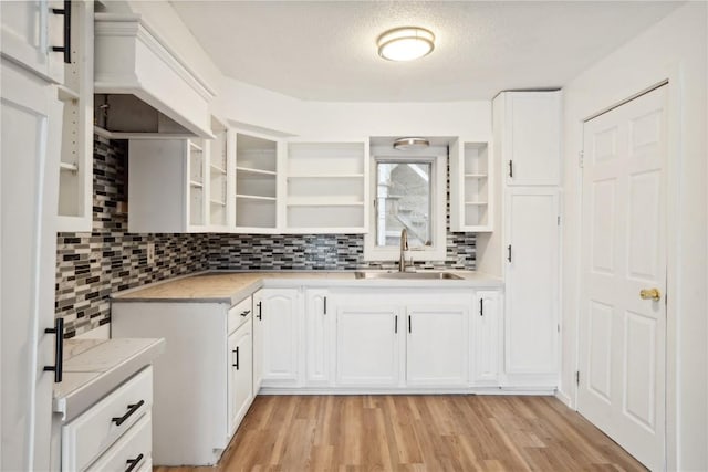 kitchen with white cabinetry, sink, tasteful backsplash, a textured ceiling, and light wood-type flooring