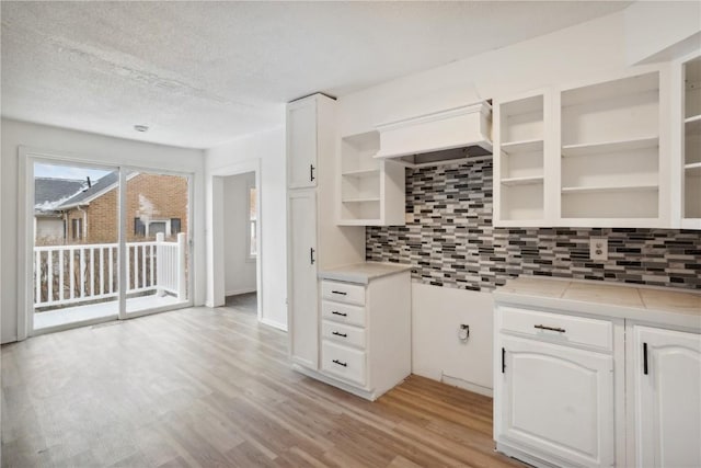 kitchen with decorative backsplash, a textured ceiling, light hardwood / wood-style flooring, white cabinetry, and tile counters