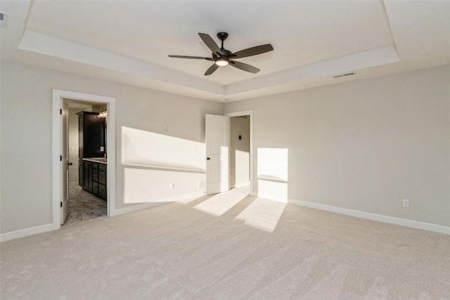 unfurnished bedroom featuring light colored carpet, a raised ceiling, ensuite bath, and ceiling fan