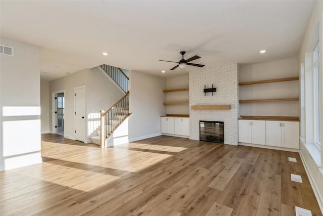 unfurnished living room with light hardwood / wood-style floors, a brick fireplace, ceiling fan, and a healthy amount of sunlight