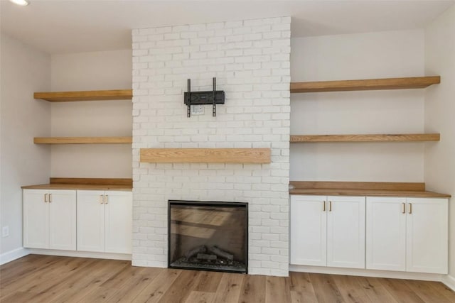 unfurnished living room with a brick fireplace and light hardwood / wood-style flooring