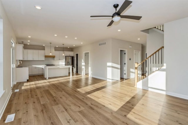 unfurnished living room with light wood-type flooring, ceiling fan, and sink