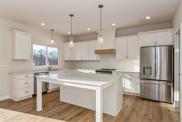 kitchen featuring appliances with stainless steel finishes, premium range hood, white cabinets, light hardwood / wood-style floors, and a kitchen island