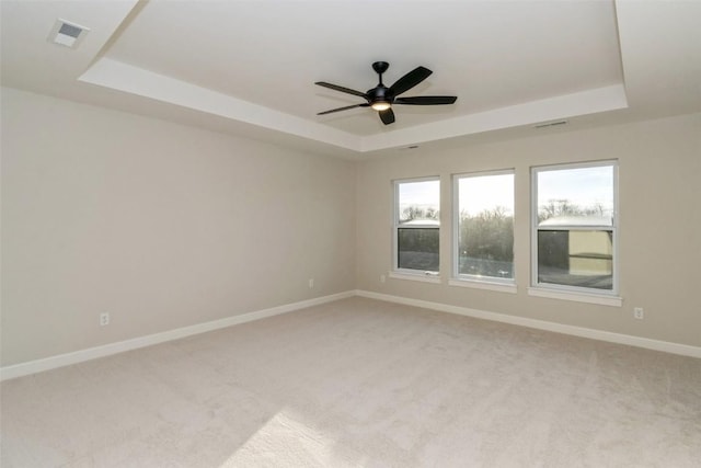 spare room with light colored carpet, a raised ceiling, and ceiling fan