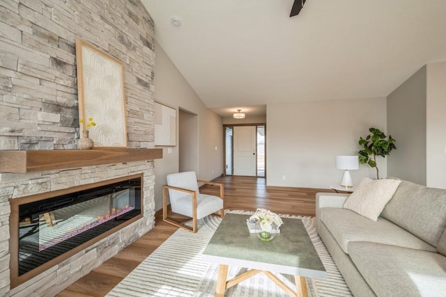 living room featuring a stone fireplace, lofted ceiling, and hardwood / wood-style flooring