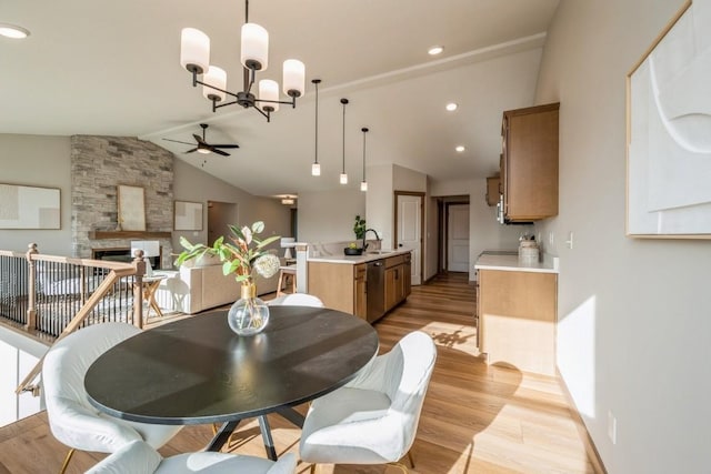 dining room with sink, a stone fireplace, light hardwood / wood-style flooring, lofted ceiling with beams, and ceiling fan with notable chandelier