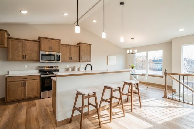 kitchen with a kitchen bar, light wood-type flooring, stainless steel appliances, a kitchen island with sink, and decorative light fixtures