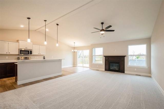 kitchen with range, a glass covered fireplace, stainless steel microwave, a wealth of natural light, and ceiling fan with notable chandelier