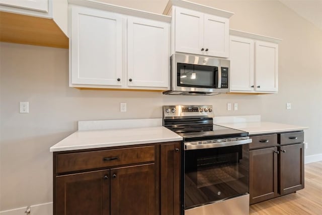 kitchen with light wood-style flooring, stainless steel appliances, dark brown cabinets, light countertops, and white cabinetry