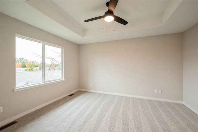 spare room featuring light carpet, a raised ceiling, visible vents, and baseboards