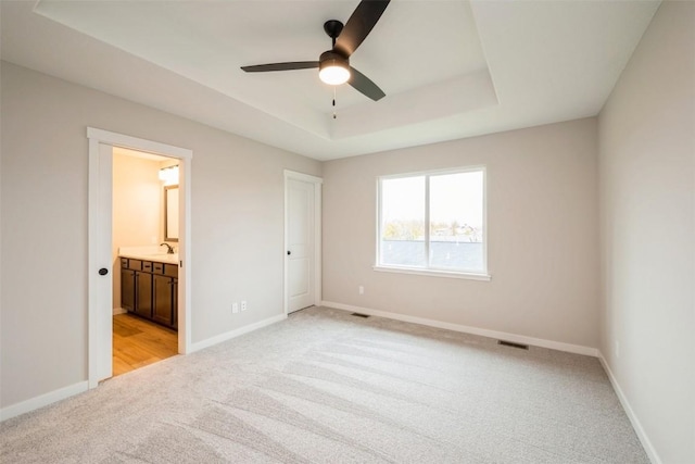 unfurnished bedroom with a raised ceiling, a sink, and baseboards