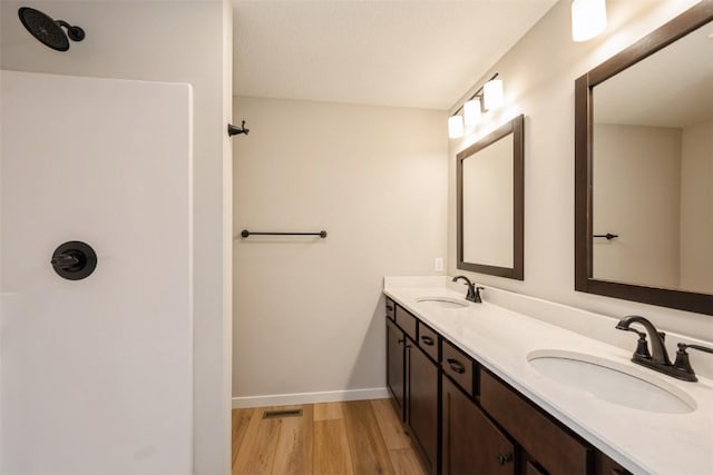 bathroom featuring double vanity, wood finished floors, a sink, and baseboards