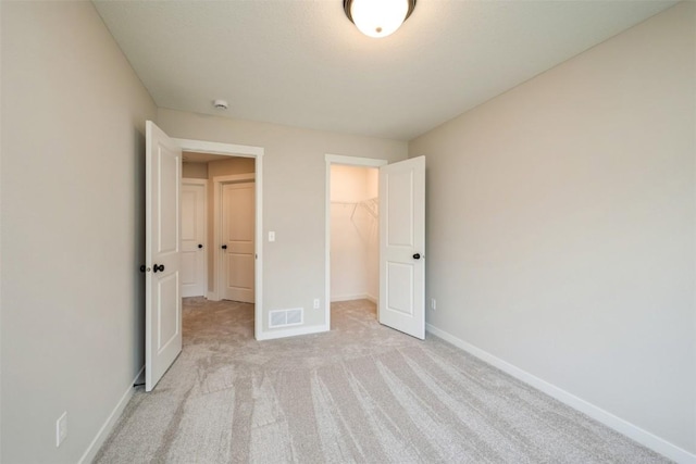 unfurnished bedroom featuring a walk in closet, a closet, light colored carpet, visible vents, and baseboards