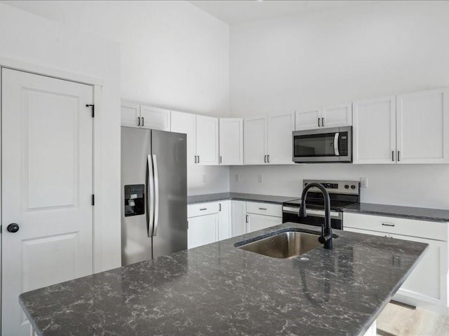 kitchen with a kitchen island with sink, sink, dark stone countertops, white cabinetry, and stainless steel appliances