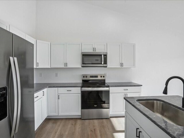 kitchen with stainless steel appliances, sink, dark stone countertops, white cabinets, and light hardwood / wood-style floors