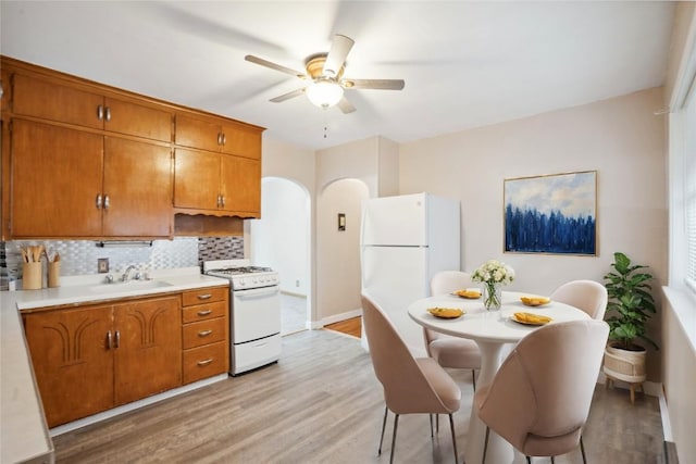 kitchen with white appliances, brown cabinetry, a sink, and backsplash