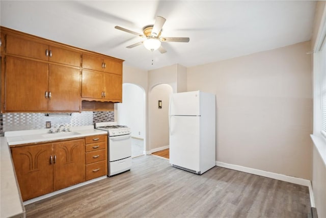 kitchen with arched walkways, white appliances, brown cabinets, and a sink