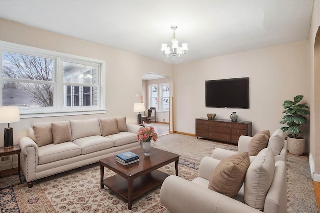 living room with a chandelier, arched walkways, light colored carpet, and baseboards