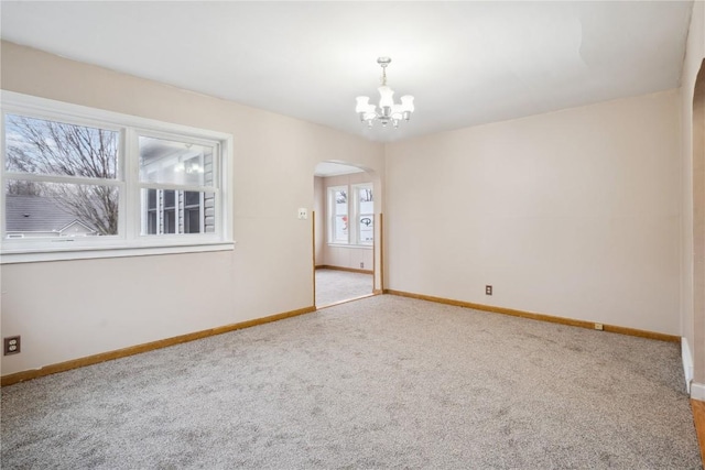 carpeted empty room with baseboards, arched walkways, and an inviting chandelier