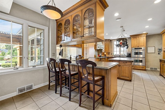 kitchen with double oven, a breakfast bar, a center island, and a healthy amount of sunlight