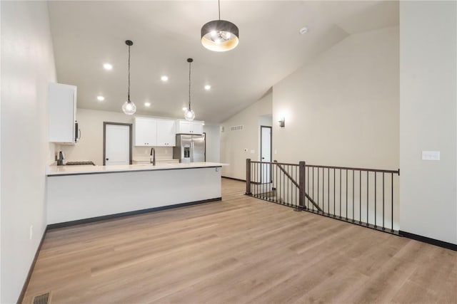 kitchen with a peninsula, stainless steel fridge, light wood-type flooring, white cabinetry, and a sink