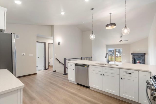 kitchen featuring ceiling fan, a stone fireplace, appliances with stainless steel finishes, a sink, and lofted ceiling